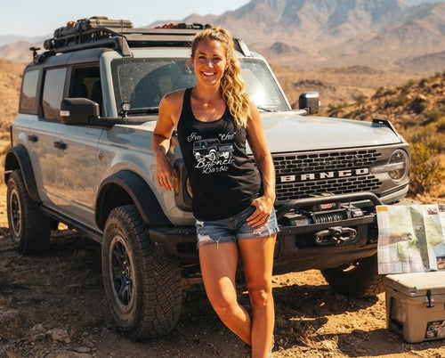 Woman wearing black Bronco Barbie tank top featuring a 1966 Bronco silhouette, posing with a 6G Bronco